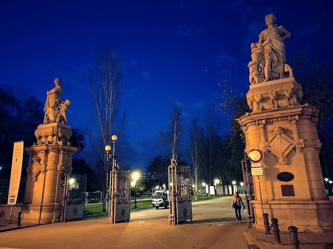 Gate piers with sculpted groups at the park's southwest entrance, lit at dusk.