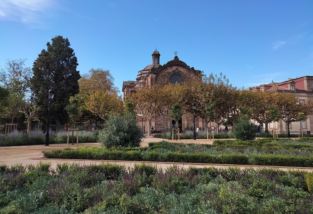 Garden beds and trees in the Ciutadella, with the old military church behind.