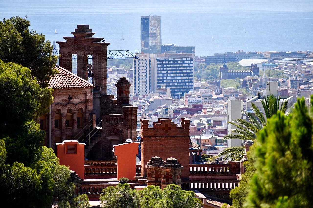 Brick-and-tile buildings at Park Güell, with the city and a tower block beyond.