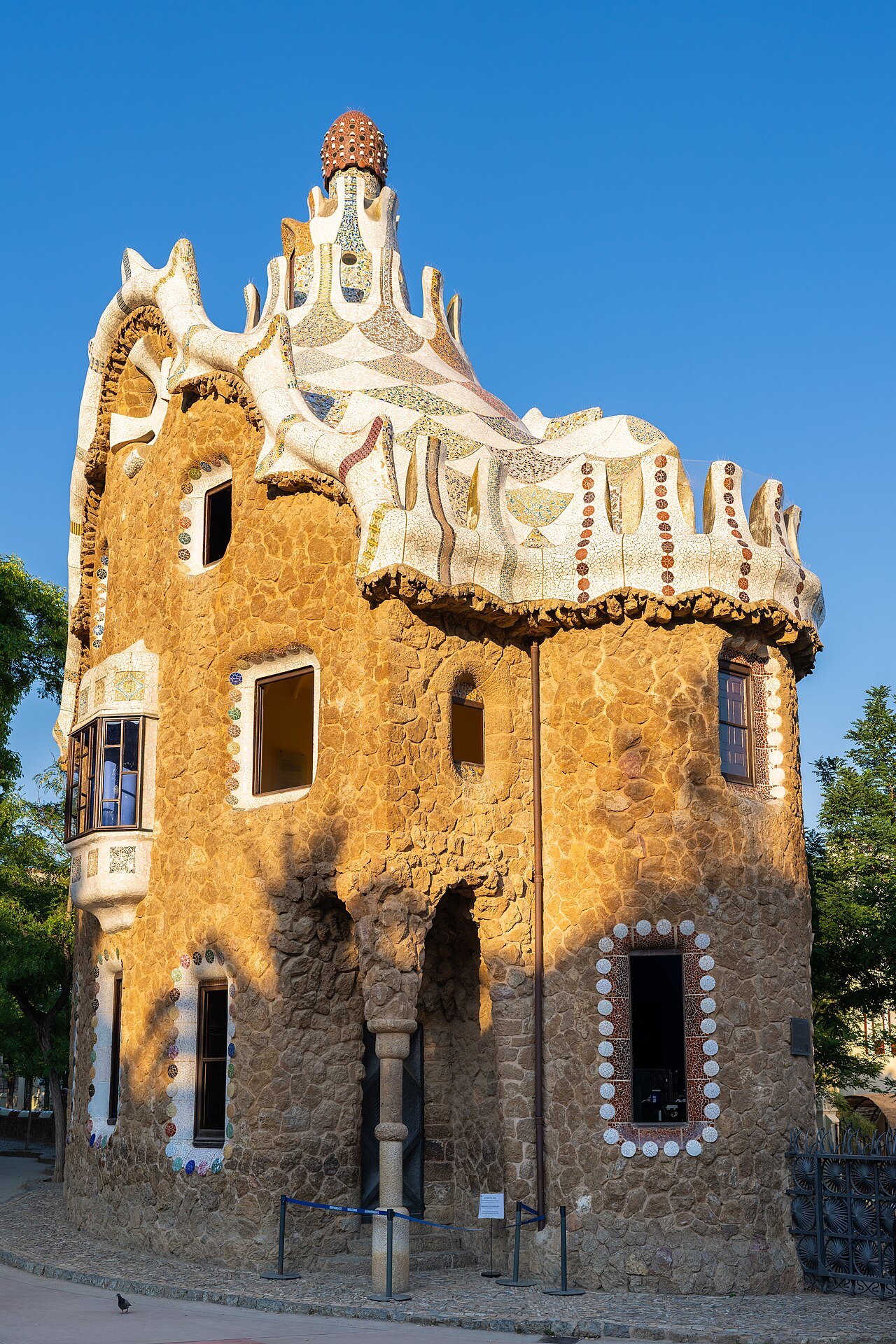 A gatehouse at Park Güell, with a wavy tiled roof and a pale crest.