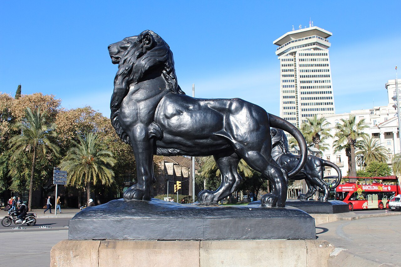 A bronze lion at the foot of the Columbus Monument, with a tower block behind.