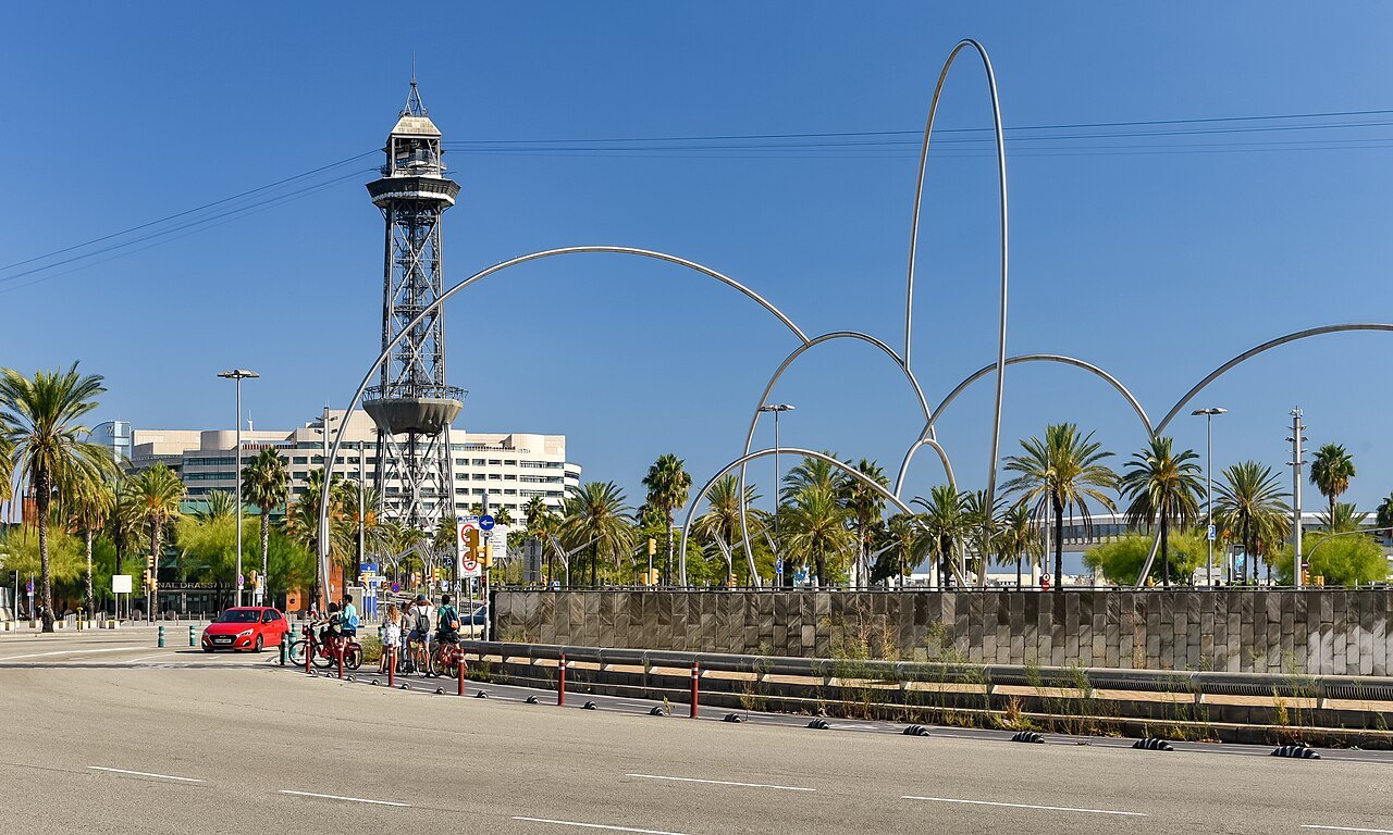 The harbor cable-car tower and a set of steel arches beside the road along the Port Vell.