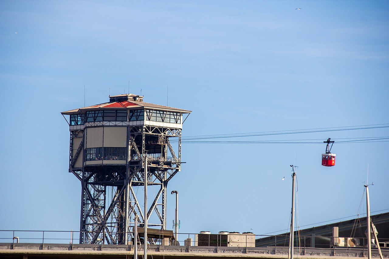 A harbor cable-car tower, with a red gondola on the wire above.