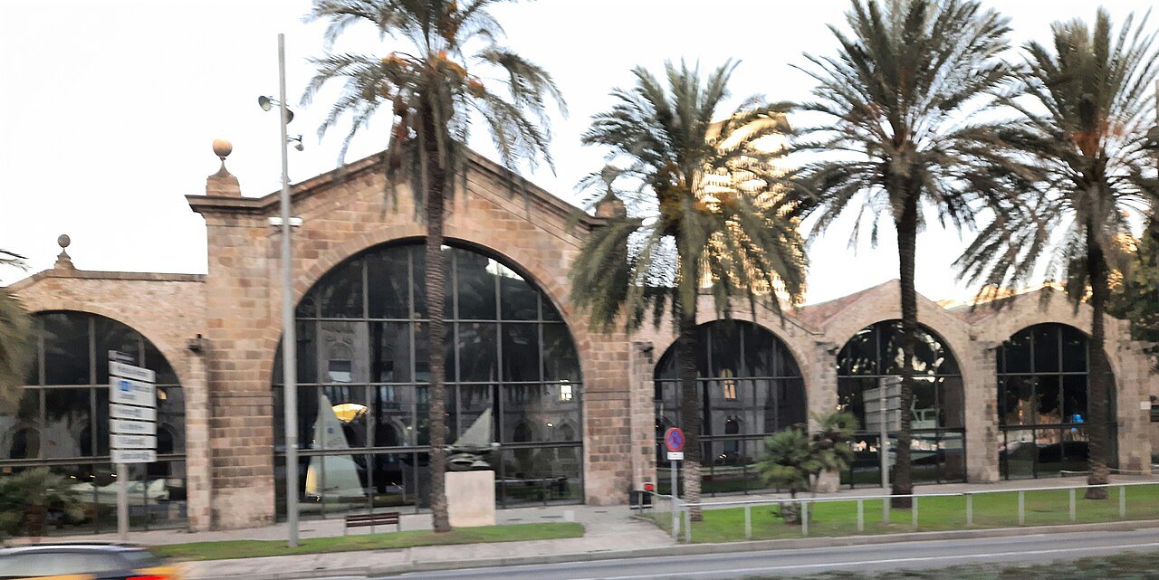 The arched halls of the medieval shipyards beyond a row of palm trees.
