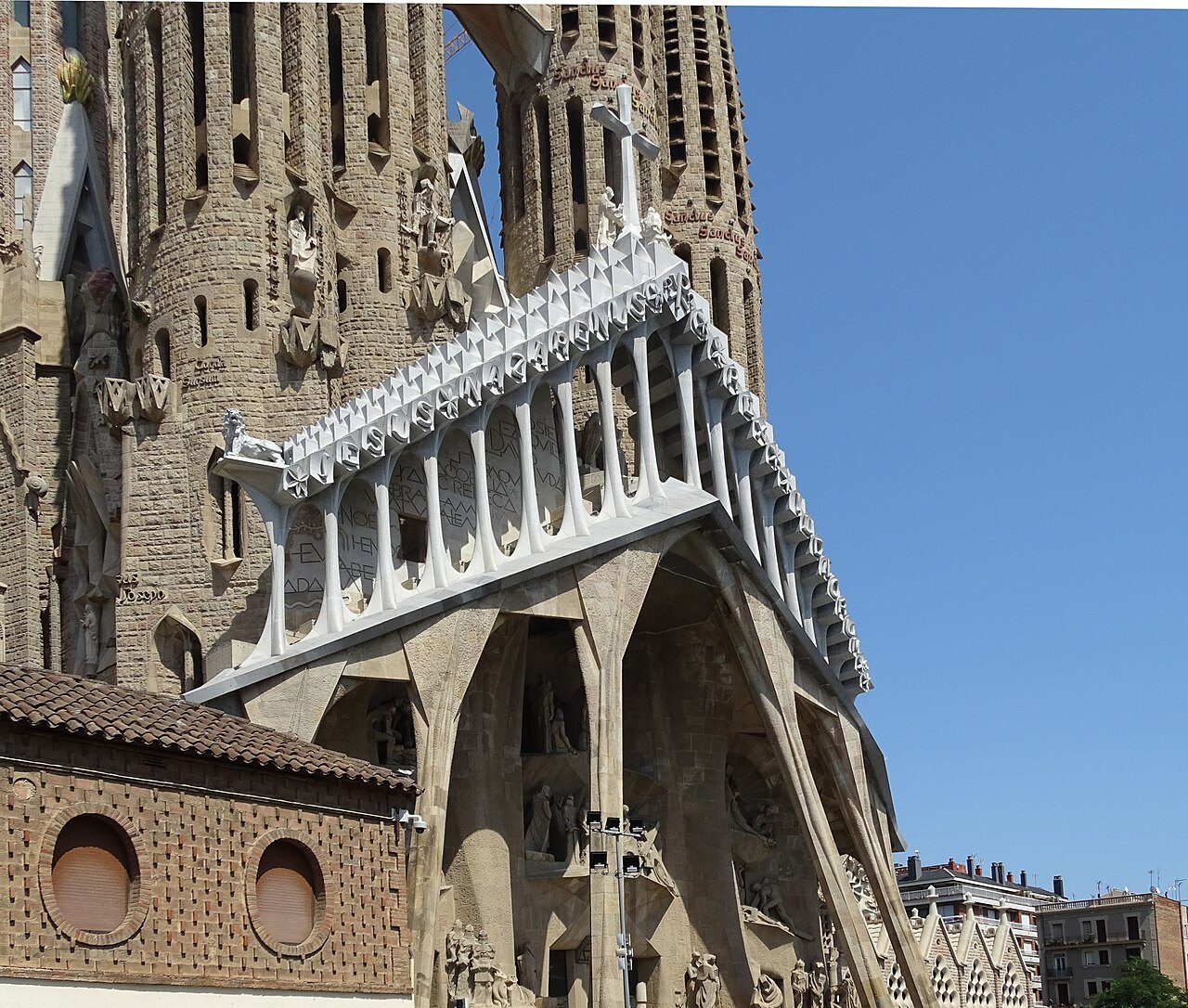 A ribbed stone bridge between two towers of the Passion façade, seen from the street.