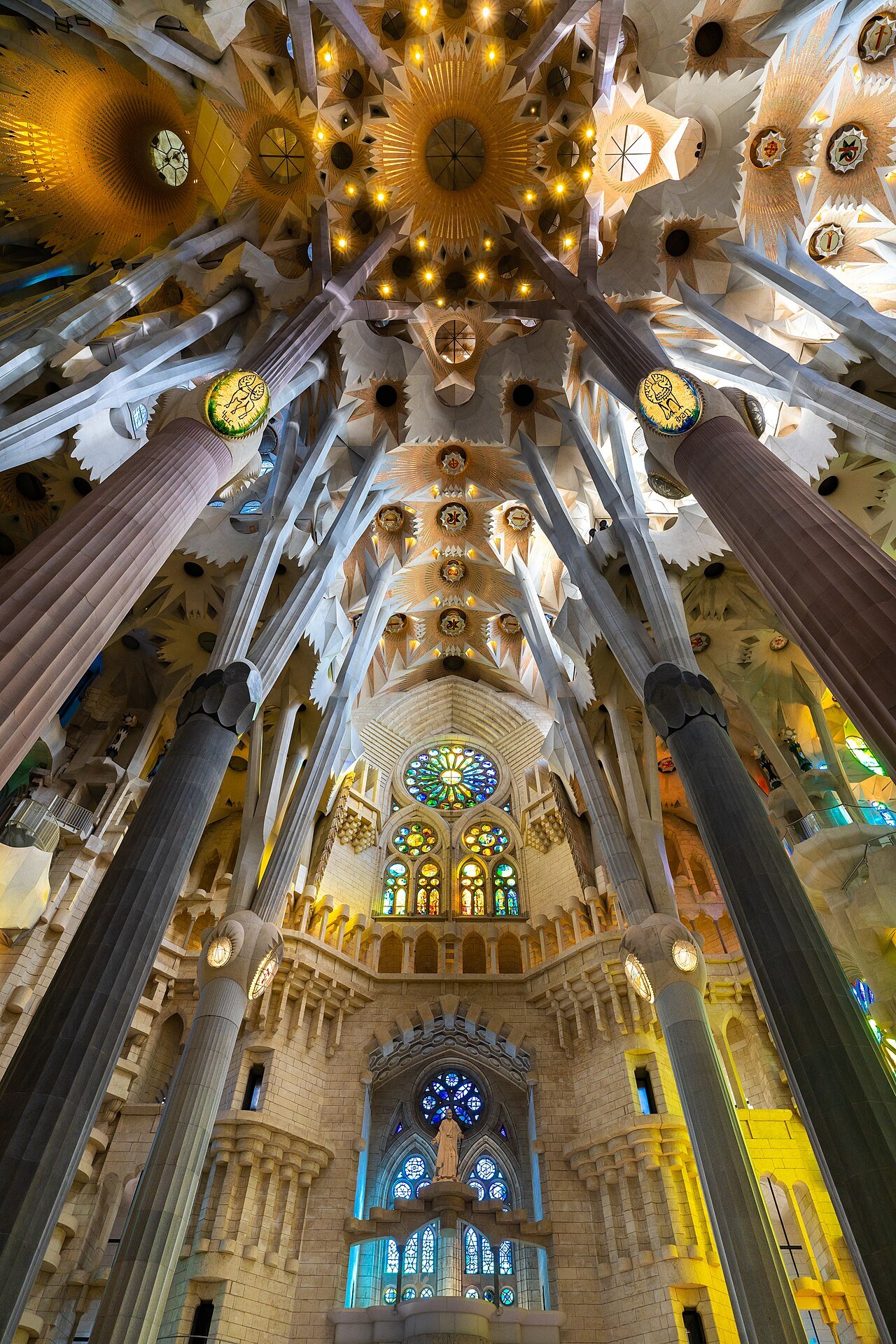 Looking up the nave of the Sagrada Família, where the columns branch toward a stained-glass window.