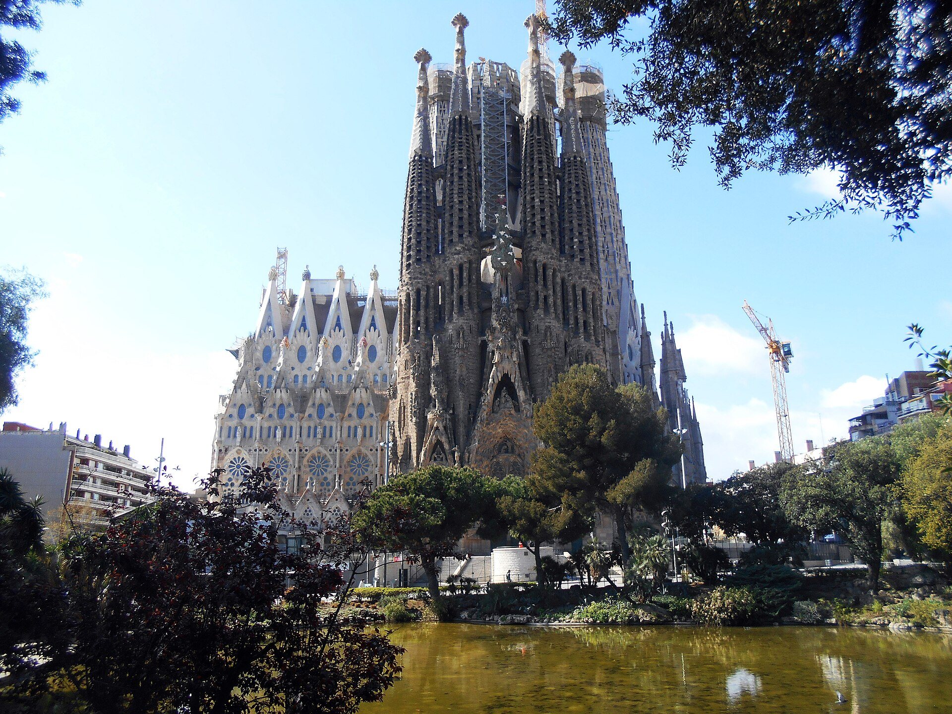 The Sagrada Família seen across the lake in the park beside it, its towers rising over the trees