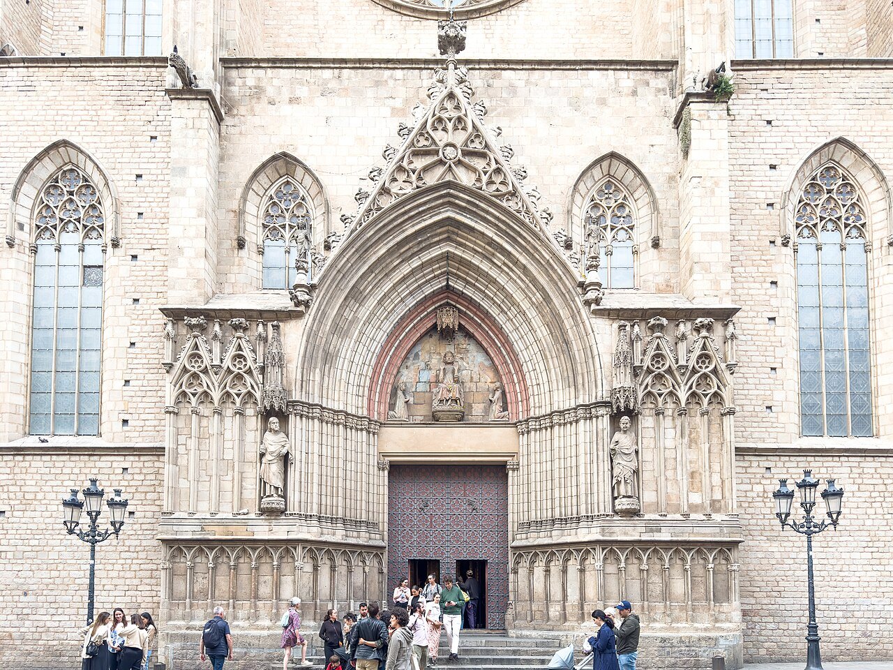 The main doorway of Santa Maria del Mar, under a Gothic arch, with visitors at the door.
