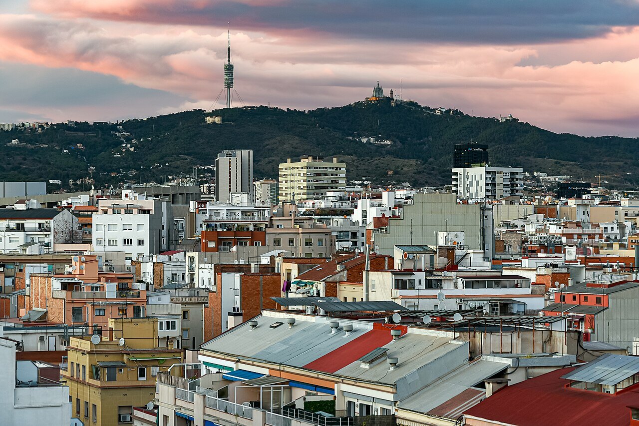 City rooftops at dusk, with the Collserola hills and the Torre de Collserola behind.