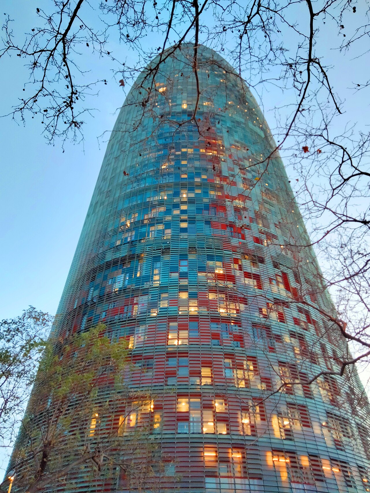 The Torre Glòries at dusk, with lit windows glowing among its colored panels.